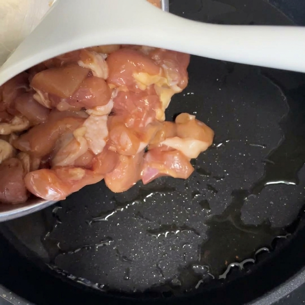 Pezzi di pollo marinato versati in una padella nera con olio caldo.