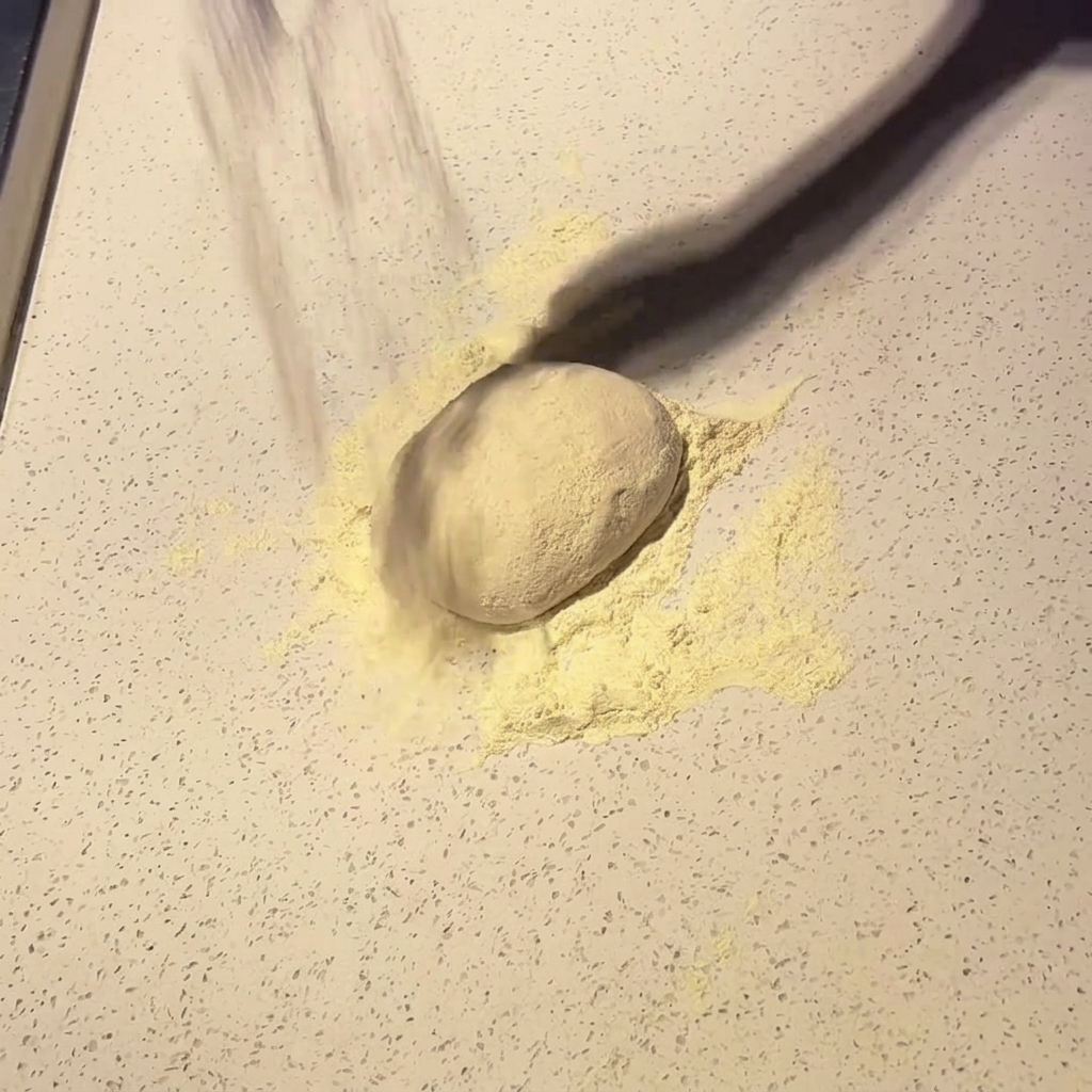Un panetto di pizza infarinato su un piano di lavoro chiaro.
