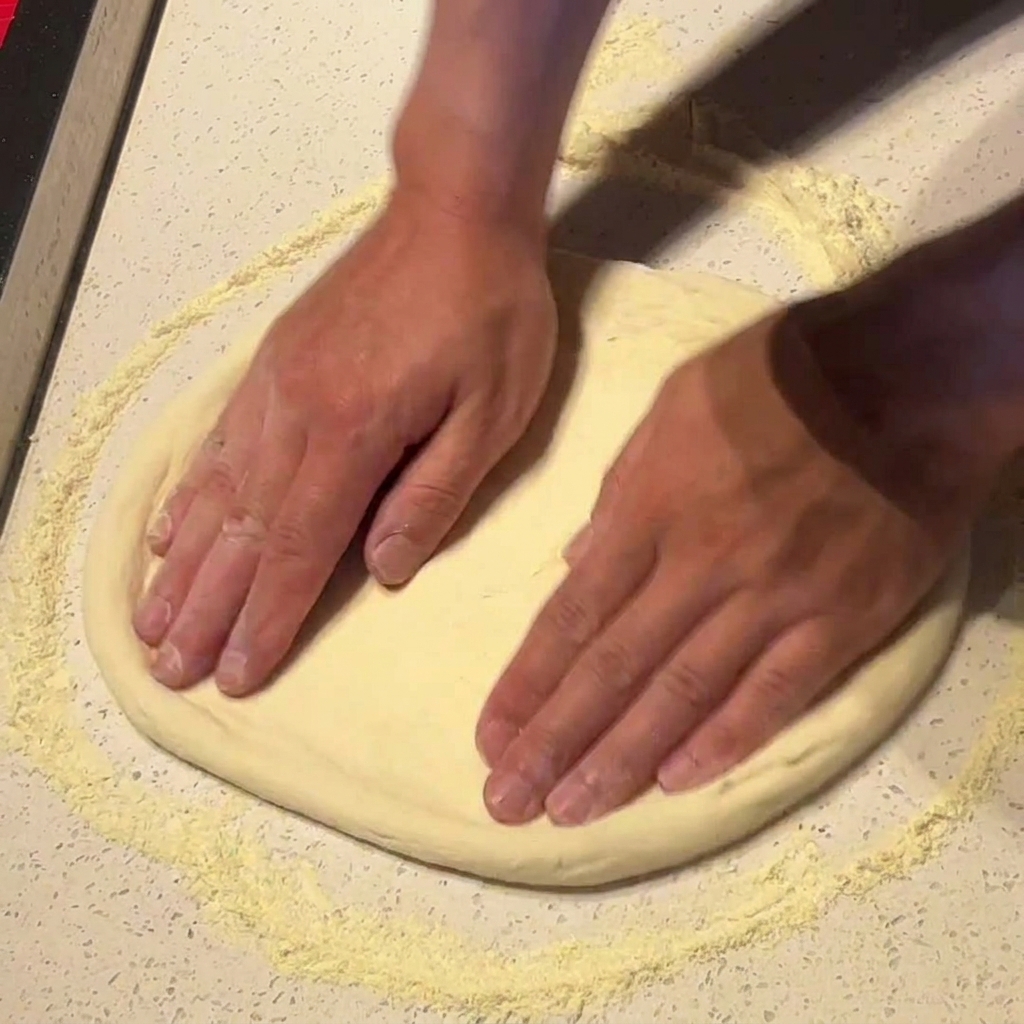 Mani che stendono e allargano la base della pizza su una superficie infarinata.