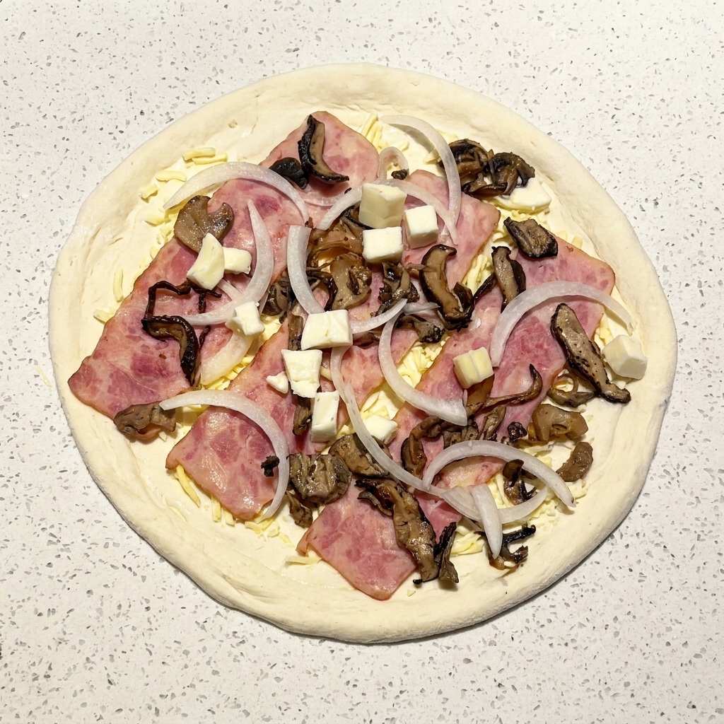 Pizza cruda assemblata condita con pancetta, funghi, cipolle e cubetti di mozzarella fresca.