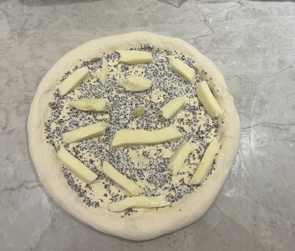 Base della pizza con salsa al tartufo e pezzi di mozzarella distribuiti sopra.