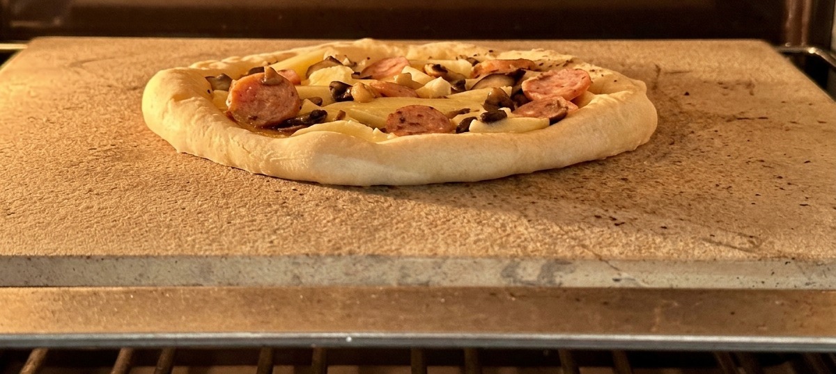 Pizza assemblata con salsiccia e funghi posizionata sulla pietra refrattaria nel forno caldo.