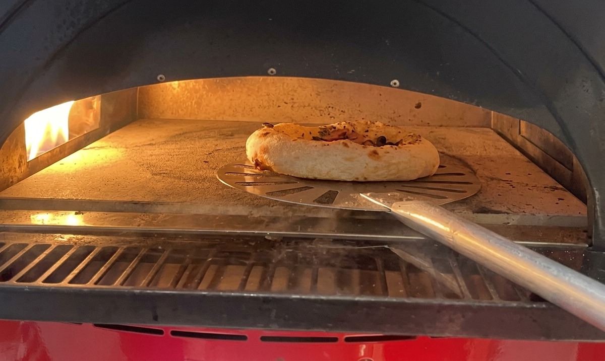 Piccola pizza con funghi e salsiccia che cuoce in forno, con il bordo che si gonfia visibilmente.