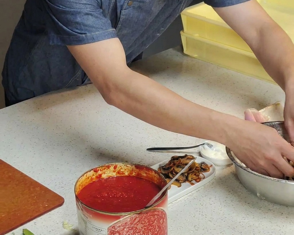 Mani di uno chef che immergono un panetto di pizza in una ciotola dacciaio piena di farina bianca.