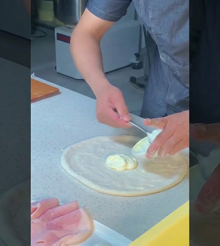 Uno chef usa il dorso di un cucchiaio per stendere uniformemente la salsa bianca sullimpasto con movimenti circolari.