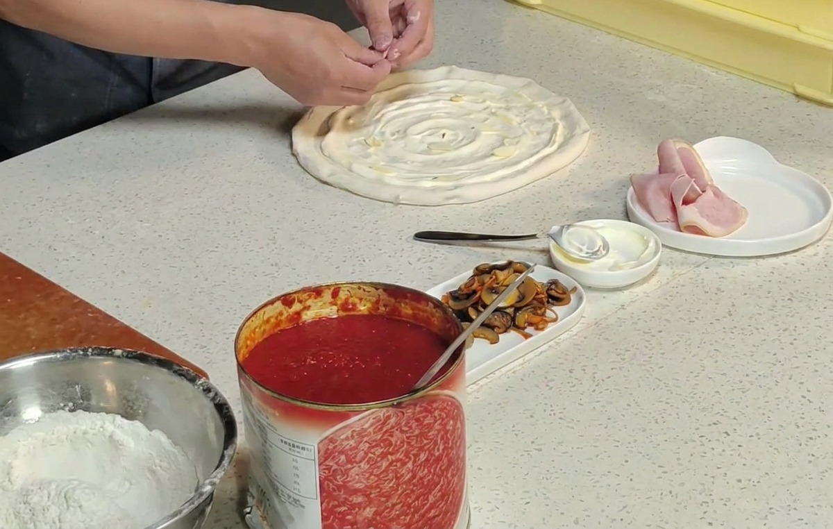Mani di uno chef che posizionano fiori di cordyceps arancioni su una base pizza cruda.
