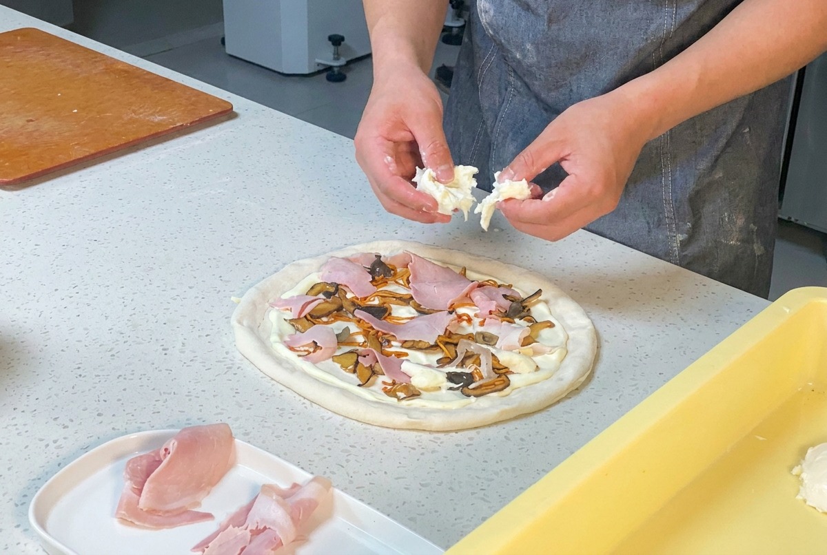 Mani di uno chef che rompono la mozzarella fresca sopra una pizza farcita.