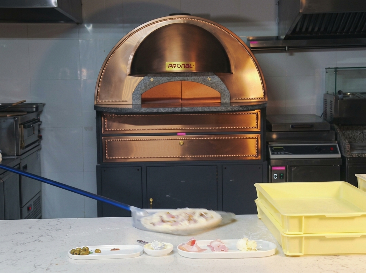 Una pizza cruda che viene inserita velocemente in un forno a cupola ardente usando una pala a manico lungo.