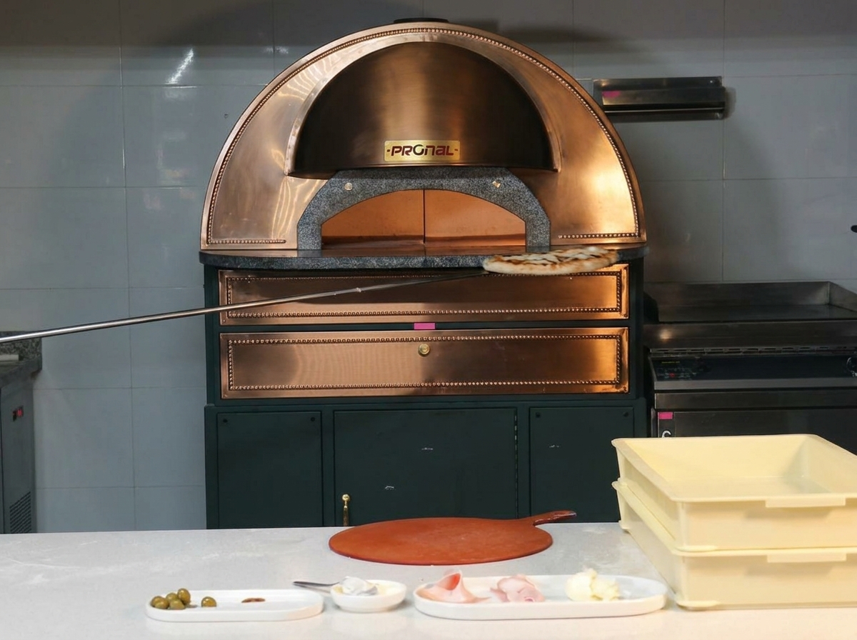 Una pizza perfettamente cotta con cornicione maculato estratta da un forno in rame con una pala metallica.