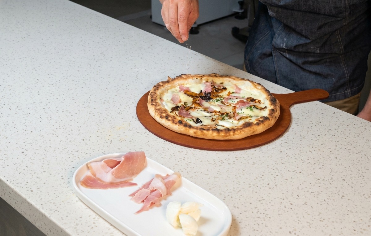 La mano di uno chef che spolvera formaggio grattugiato su una pizza calda appena sfornata.