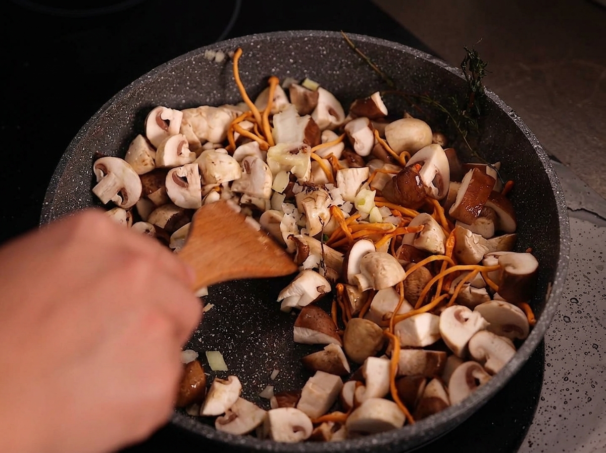 Spatola di legno che mescola cipolla tritata e aglio a fette in una padella di funghi già cotti.