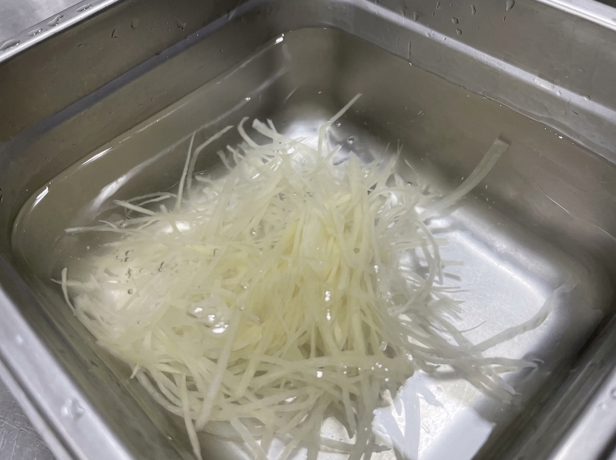 Fiammiferi di patate immersi in un contenitore dacciaio con acqua limpida.