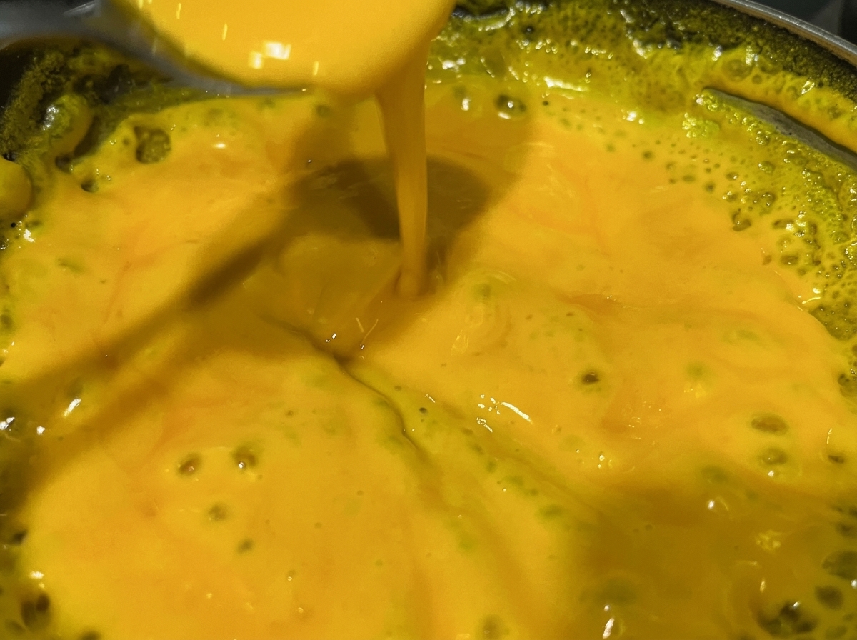 Un cucchiaio che mescola una salsa al formaggio gialla e densa in un pentolino.