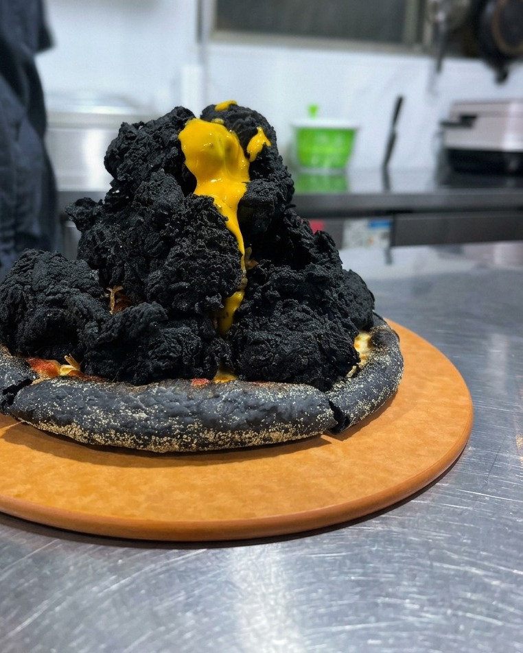 Salsa al formaggio gialla che cola come lava lungo una montagna di pollo fritto nero su una pizza.