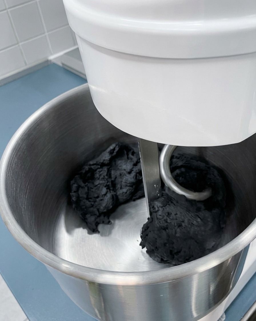 Primo piano del gancio dellimpastatrice che lavora una massa di impasto nero profondo.