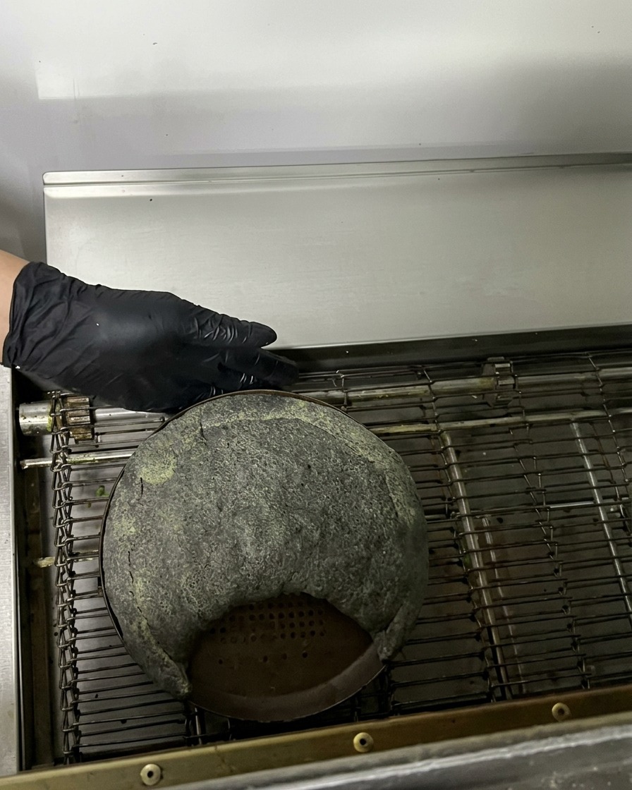 Un calzone nero crudo su una teglia che entra in un forno a nastro professionale.