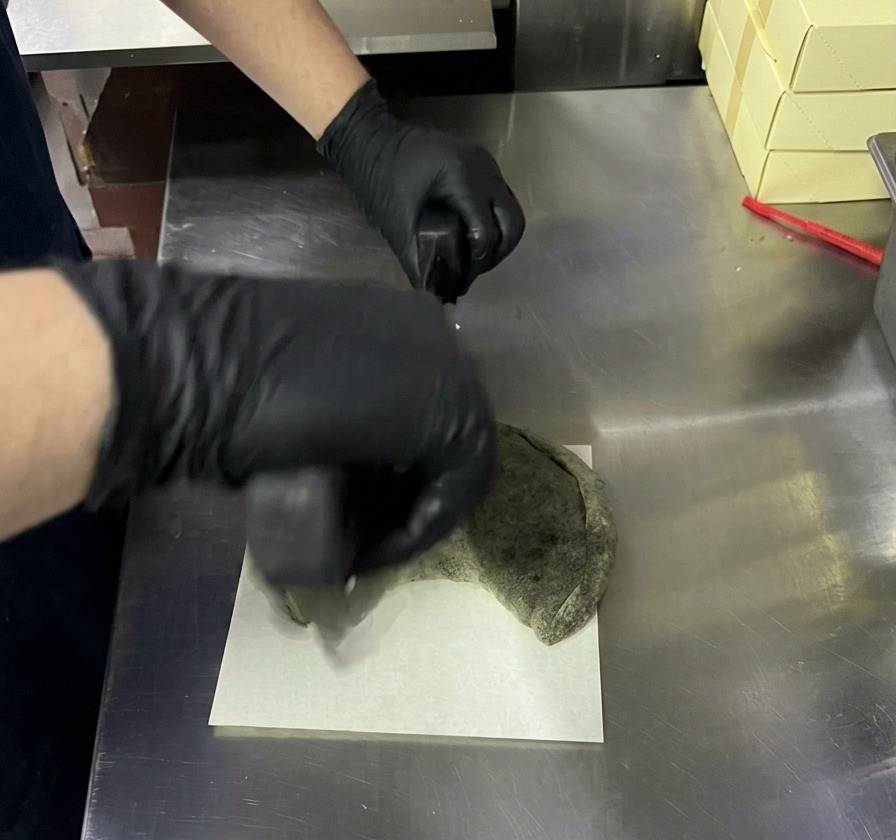 Taglio di un calzone nero cotto con una lama rotante per pizza su un tagliere bianco.