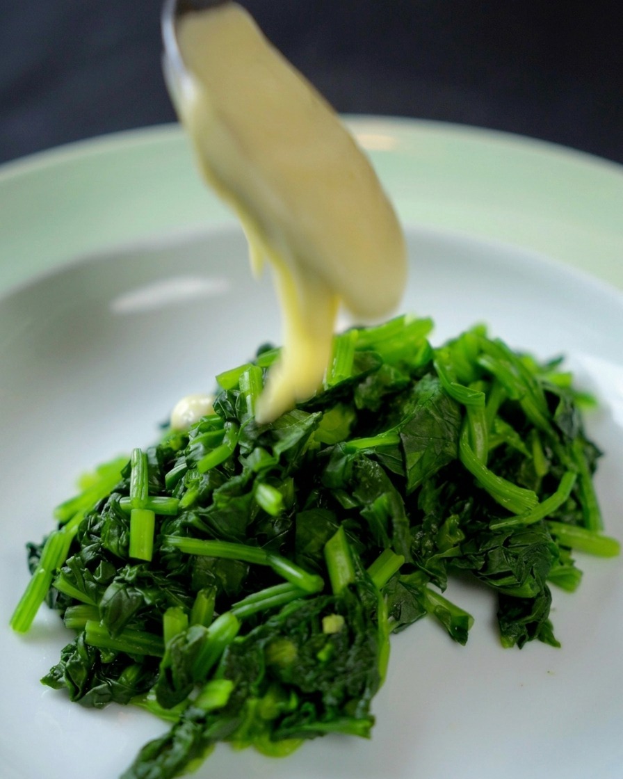 Salsa bianca versata sopra un mucchietto di spinaci tritati in una ciotola.