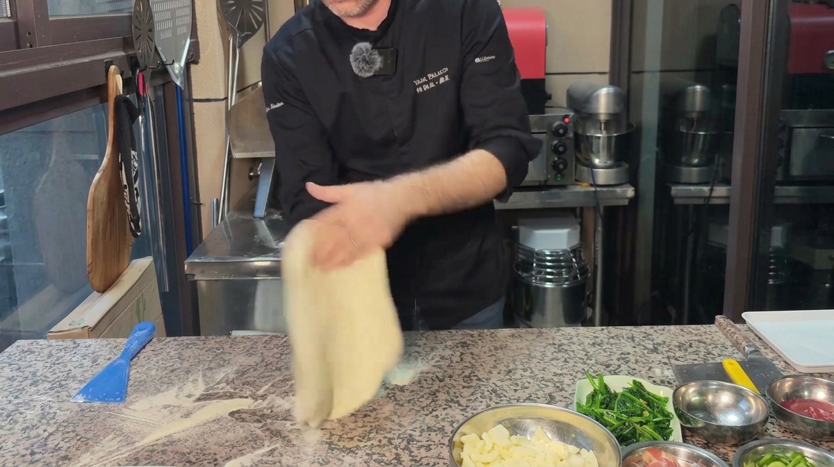 Uno chef che stende limpasto per pizza in un cerchio su una superficie di marmo infarinata.