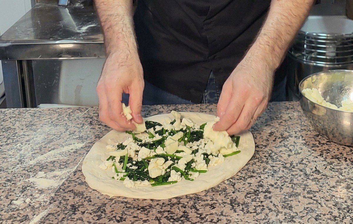 Aggiunta di pezzi di mozzarella sopra gli spinaci e la feta su una pizza cruda.