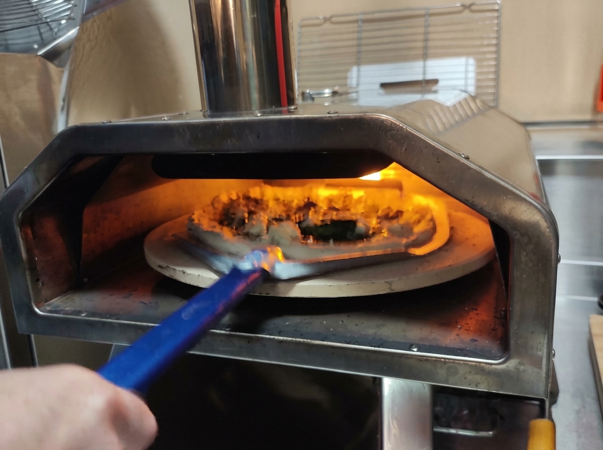 Utilizzo di una pala per pizza forata per sollevare una pizza cruda e inserirla in un forno ardente.