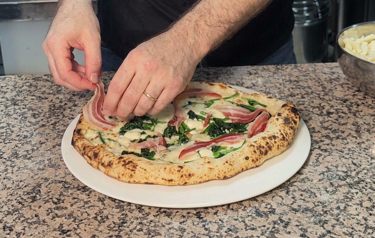 Fette di pancetta adagiate sopra una pizza calda appena sfornata con spinaci e formaggio.