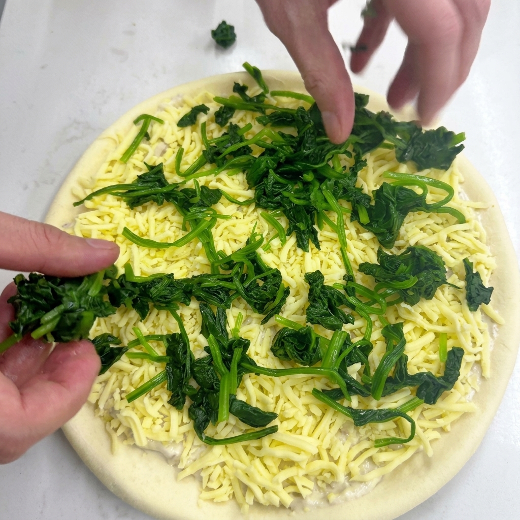 Due mani che posizionano piccoli mucchietti di spinaci verdi sulla mozzarella.