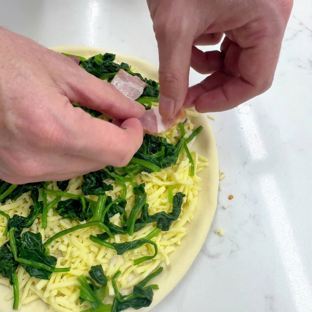 Mani che posizionano fettine rettangolari di pancetta cruda sulla pizza con spinaci e mozzarella.