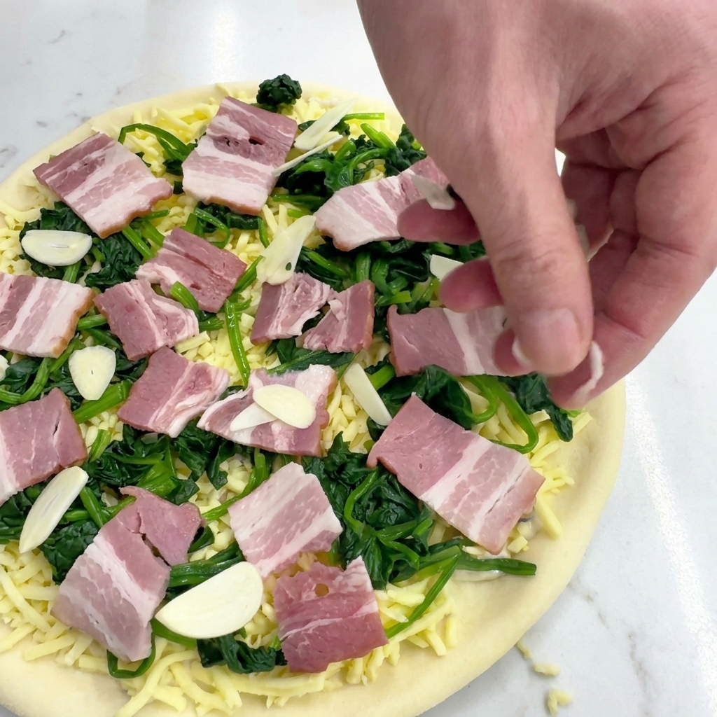 Una mano che sparge fettine sottili di aglio crudo su una pizza condita con spinaci e pancetta.