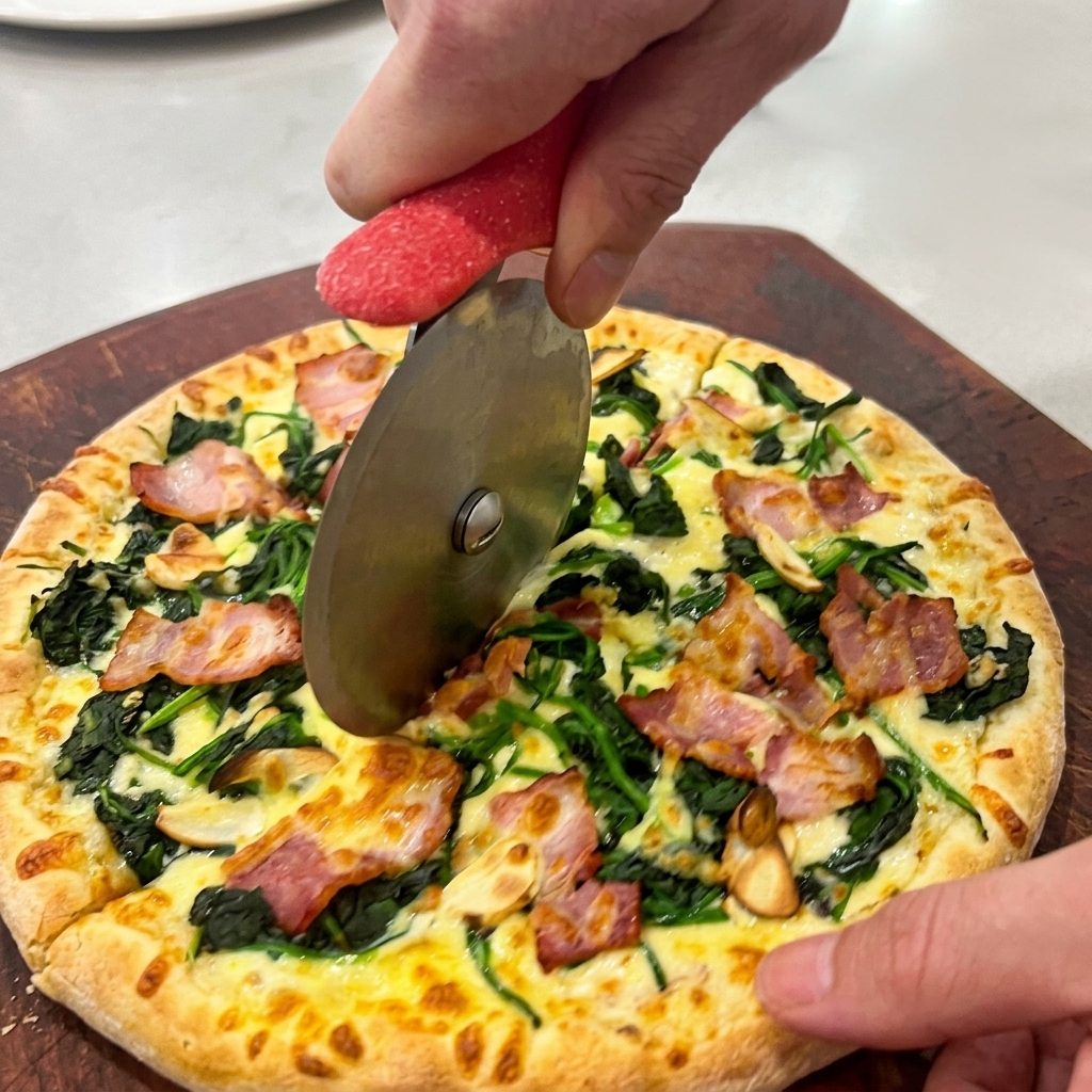 Mani che usano una rotella tagliapizza per dividere la pizza calda su un tagliere di legno.