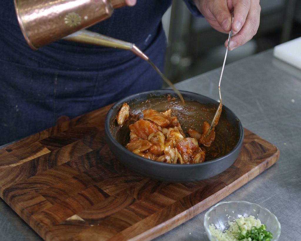 Mani che versano un filo dolio doliva da un oliatore in rame in una ciotola di frutti di mare marinati.