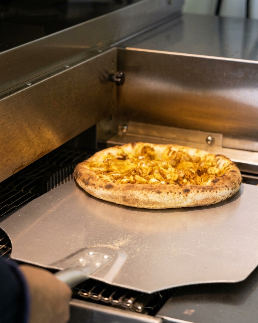 Una pizza ai frutti di mare appena sfornata con il bordo leggermente bruciacchiato prelevata con una pala metallica.