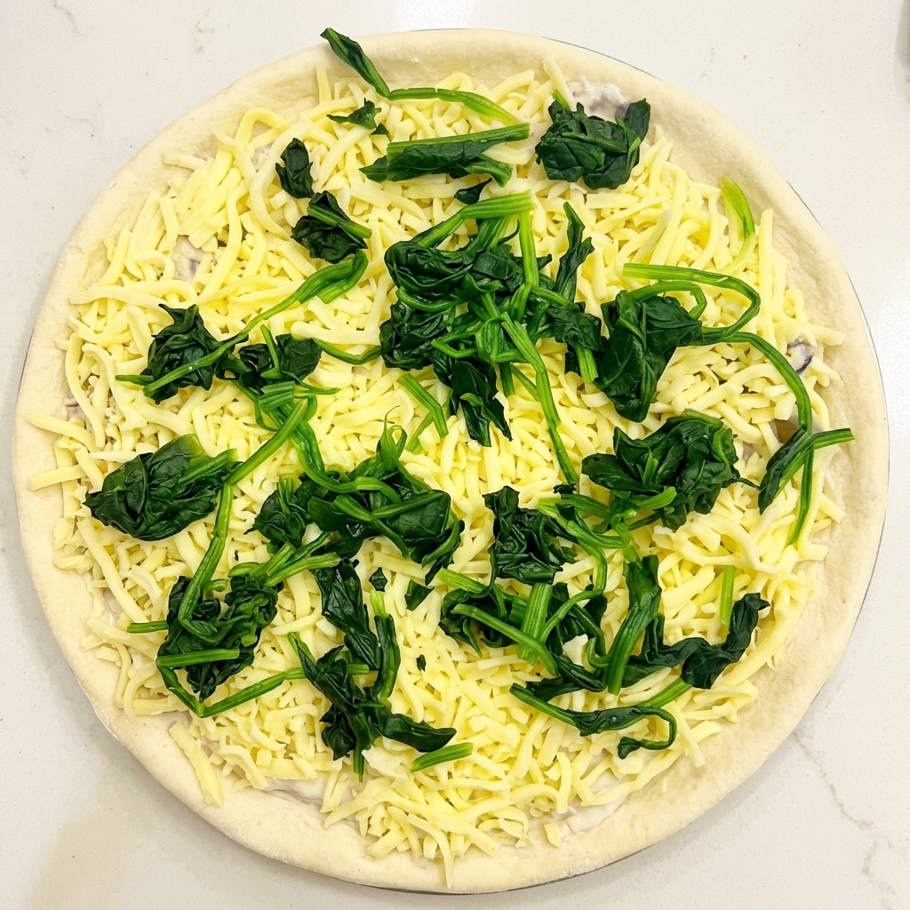 Vista dallalto di una pizza cruda condita con salsa, mozzarella e piccoli mucchietti di spinaci verdi sbollentati.