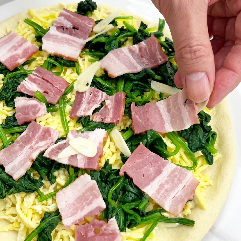 Mani che distribuiscono fette sottili di aglio crudo su una pizza ricoperta di mozzarella, spinaci e pancetta.