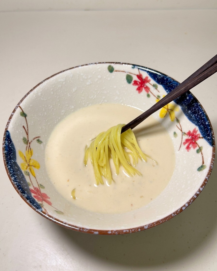 Noodles gialli cotti inseriti nel brodo cremoso allinterno di una ciotola decorativa.