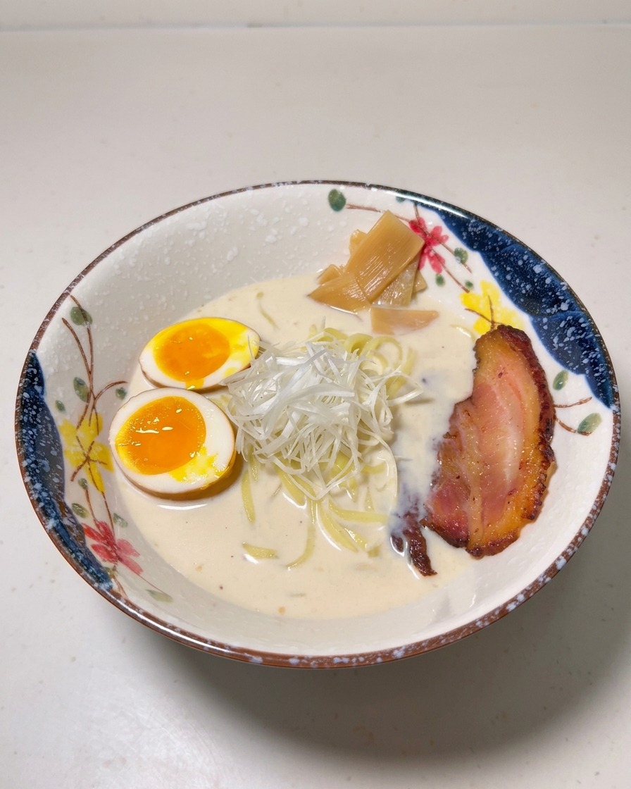 Una ciotola di ramen guarnita con uova barzotte, bambù, cipollotti bianchi e una fetta di maiale chashu rosolato.