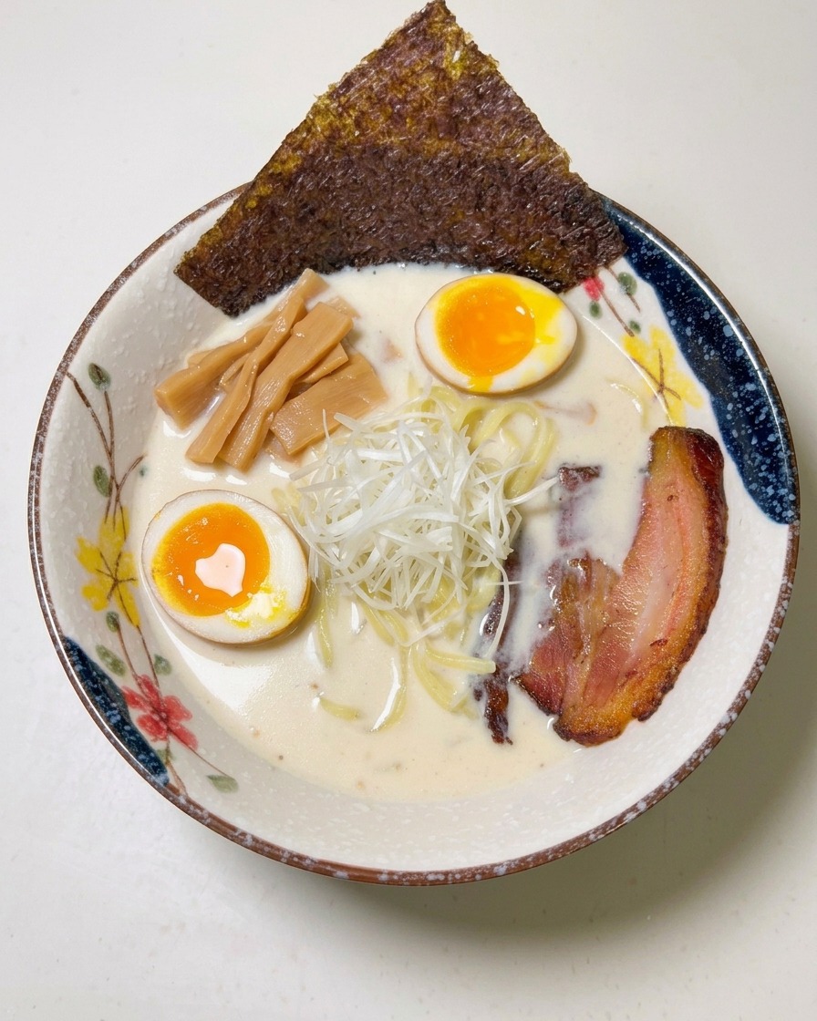 Un foglio di alga nori scura infilato sul bordo di una ciotola di ramen completa.