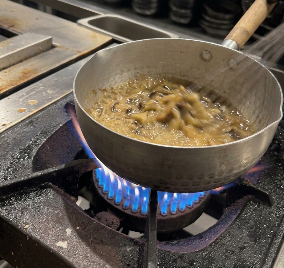 Una frusta mescola continuamente una salsa densa e marrone scuro in una pentola.