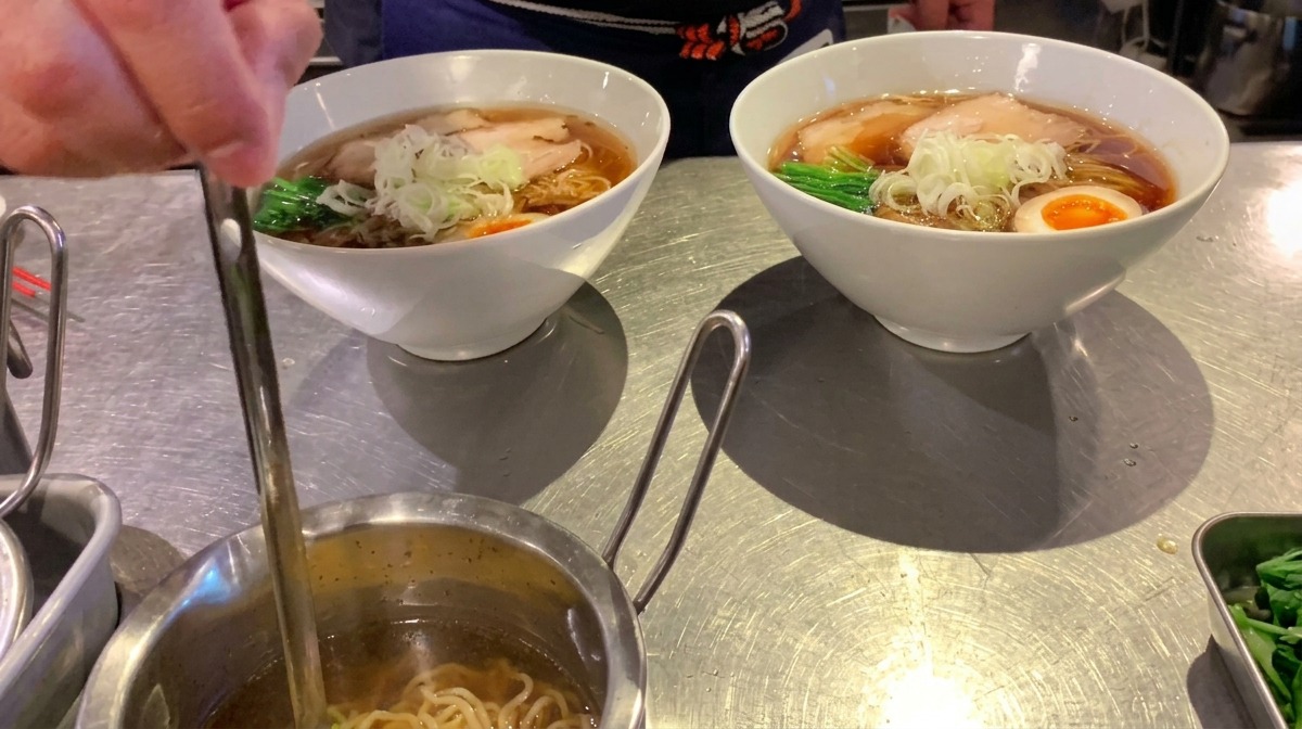 Un piccolo mestolo che versa olio aromatico limpido su una ciotola di ramen completata.