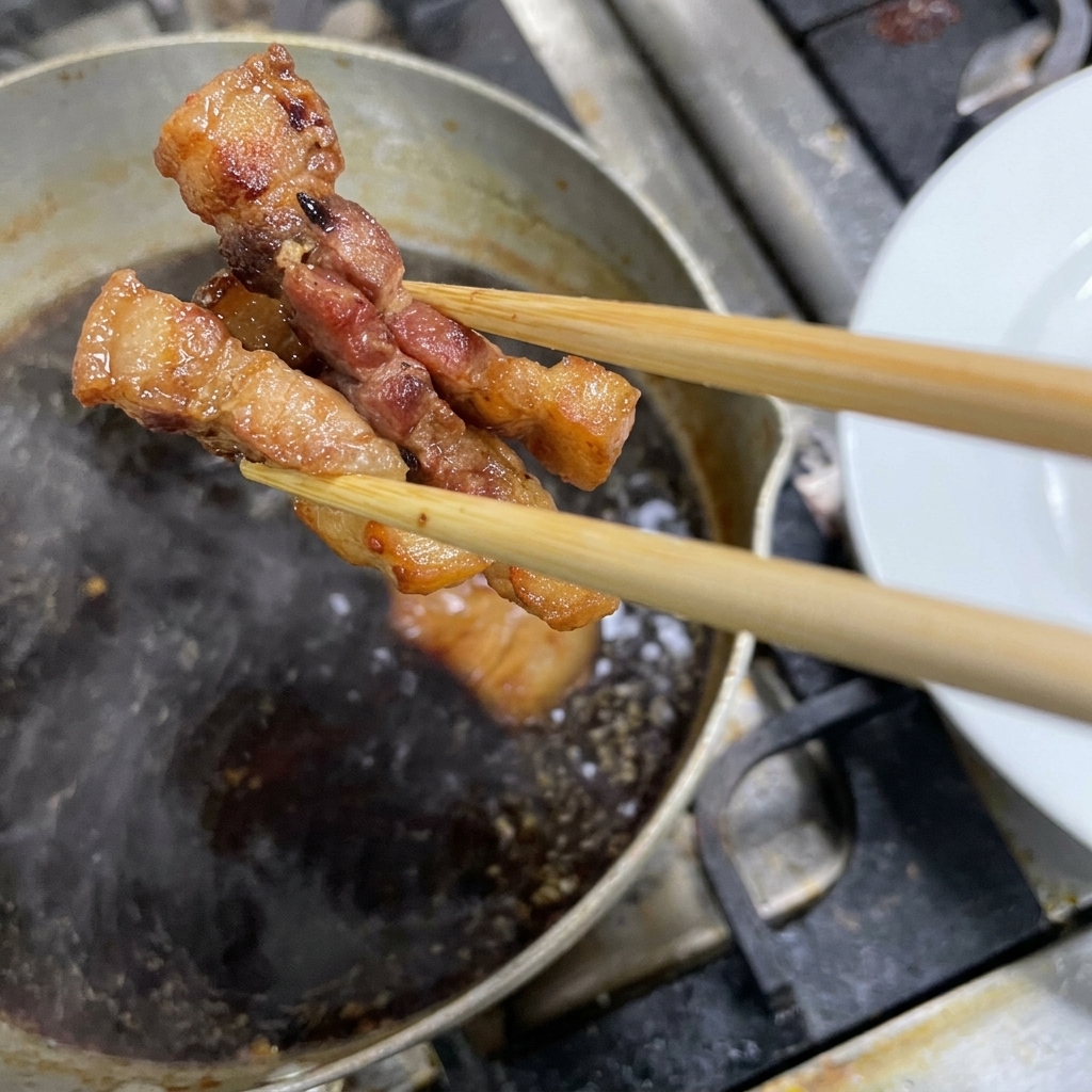 Bacchette che prelevano pezzi scuri di pancetta di maiale brasata da una pentola con salsa a fuoco lento.