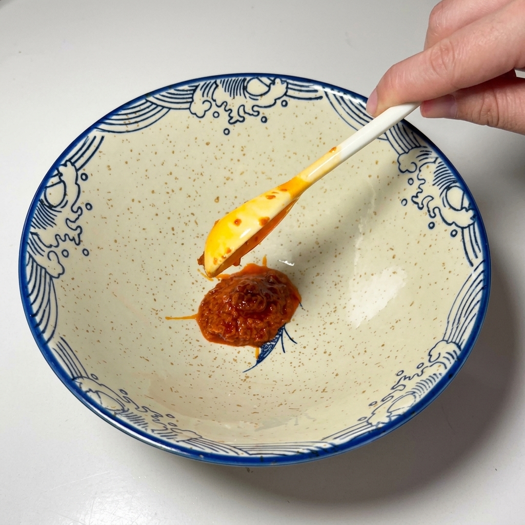 Un cucchiaio di pasta di peperoncino rossa posizionato in una ciotola di ceramica vuota.