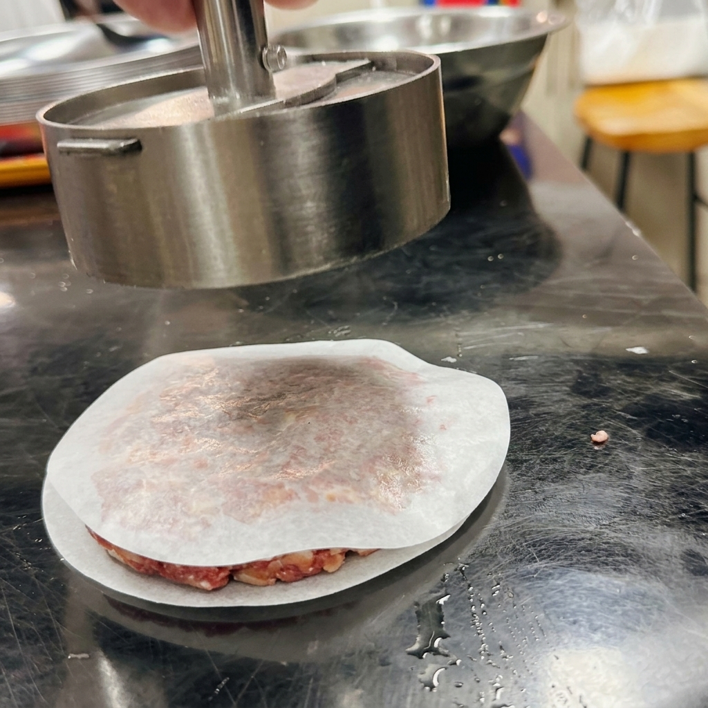 Una pressa per hamburger in metallo che modella la carne sopra un foglio di carta forno.
