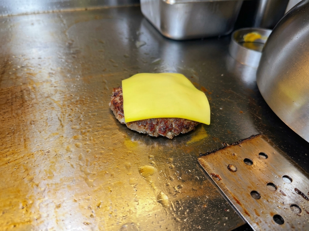 Una fetta di formaggio giallo che inizia a sciogliersi sopra lhamburger sulla piastra.
