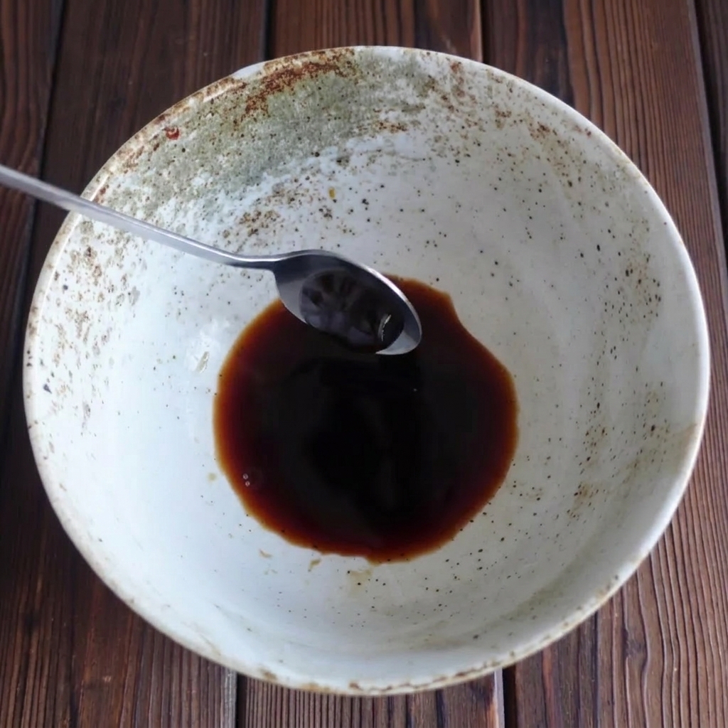 Un cucchiaio di metallo che aggiunge salsa dostriche densa in una ciotola con salsa di soia.