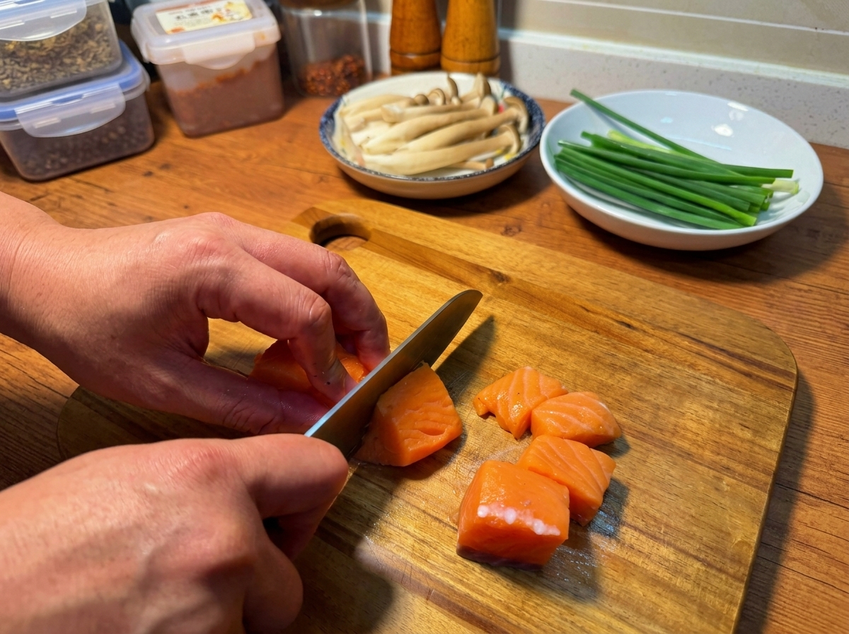 Mani che usano un coltello per tagliare un filetto di salmone fresco a cubetti uniformi su un tagliere di legno.