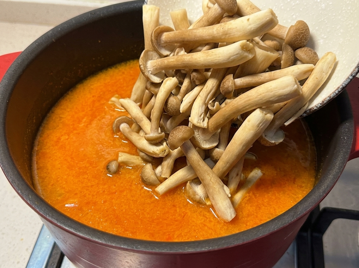 Funghi shimeji freschi versati da una ciotola in una pentola di brodo arancione al miso.