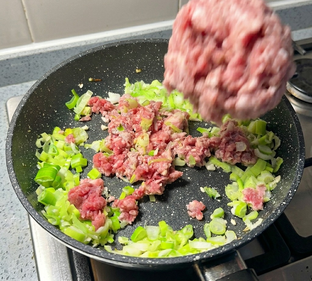 Maiale macinato aggiunto in padella insieme ai cipollotti.