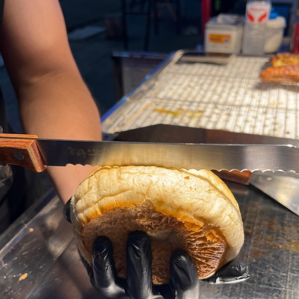 Una mano che usa un coltello seghettato per tagliare delicatamente a metà orizzontalmente un panino al sesamo.