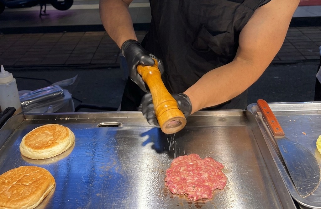 Macinatura di sale marino fresco e pepe nero su un patty di manzo che sfrigola sulla piastra.