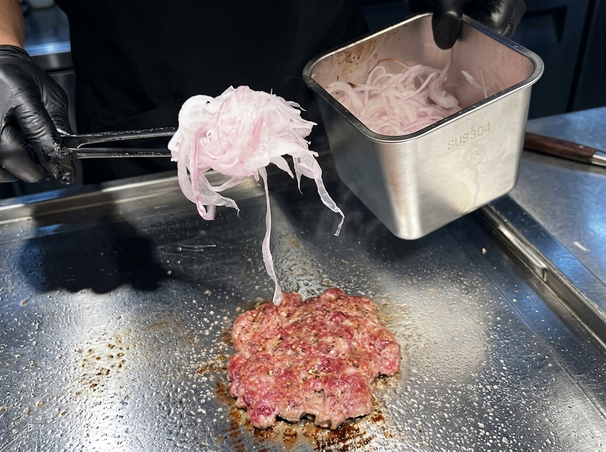 Una manciata di cipolle rosse tagliate molto sottili poste sopra il burger in cottura sulla piastra.